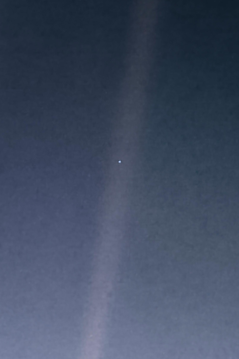 Pale Blue Dot: Earth as a single bright point inside a band of scattered sunlight, photographed by Voyager 1 in 1990.